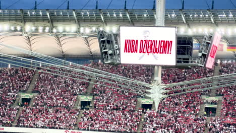 Stadium-crowd-with-a-large-screen-displaying-a-message-of-support
