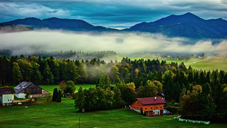 Zeitraffer-Von-Nebel,-Der-über-Eine-Lebendige-Herbstlandschaft-Mit-Rustikalen-Häusern-Und-Bewaldeten-Hügeln-Rollt