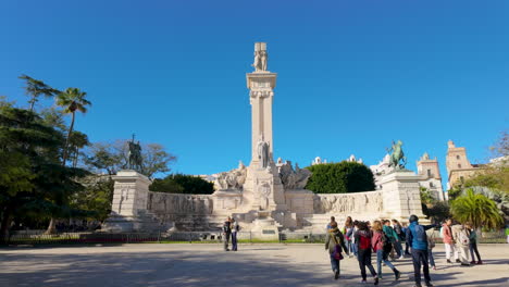 Monumental-column-and-statues-in-a-sunny-square-with-palm-trees-and-tourists