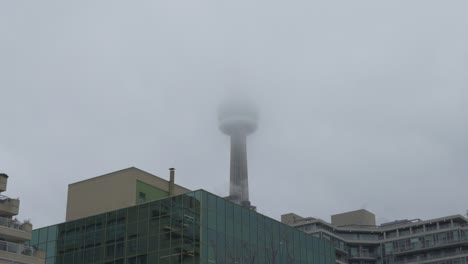CN-Tower-in-Toronto,-Canada-looming-over-buildings,-partially-obscured-by-fog,-creating-a-moody-urban-scene
