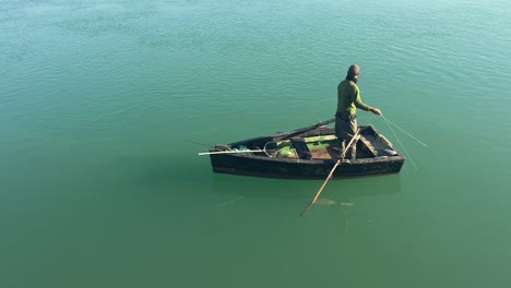 Fisherman-standing-in-boat,-calm-green-waters