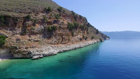 Retreating-zipline-drone-shot-along-the-rocky-coastline-of-a-secret-beach-in-Agriosiko,-located-in-Cephalonia-off-the-coast-of-Greece