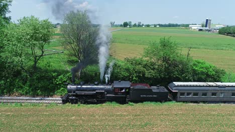 An-Aerial-Side-View-of-a-Steam-Passenger-Train,-Stopped-Traveling-Thru-Harvested-Farmlands-on-a-Sunny-Day-in-Slow-Motion