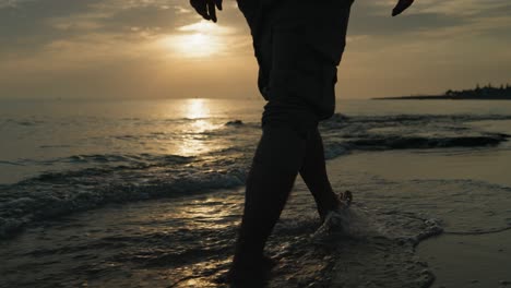 Mid-shot-of-Male-walking-on-the-beach-in-the-water-at-sunrise-away-from-the-camera-slow-motion