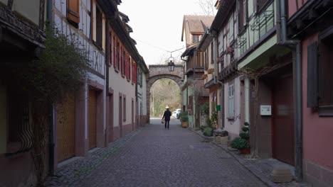 Person-walking-through-the-cobblestone-street-with-half-timbered-architectural-houses-in-Kaysersberg,-France