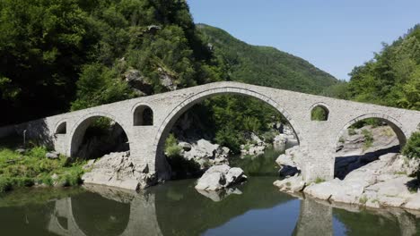 Sich-Zurückziehende-Drohnenaufnahme,-Die-Die-Länge-Der-Teufelsbrücke-Und-Des-Flusses-Arda-In-Der-Stadt-Ardino-In-Der-Nähe-Des-Rhodopengebirges-In-Bulgarien-Zeigt