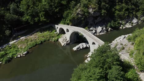 Approaching-drone-shot-moving-overhead-of-the-Devil's-Bridge-and-the-Arda-River,-located-in-the-town-of-Ardino-at-the-foot-of-Rhodope-Mountains-in-Bulgaria