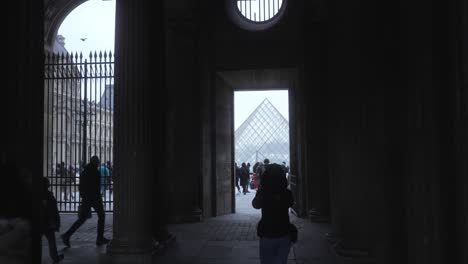 People-walking-through-building-doorway-towards-the-Louvre-museum-Pyramid-on-the-square-in-Paris