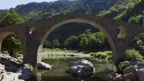 Approaching-drone-shot-passing-through-the-main-arch-of-the-Devil's-Bridge-over-the-Arda-River-located-in-the-town-of-Ardino-near-the-Rhodope-Mountains-in-Bulgaria
