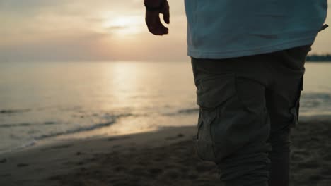Mid-shot-of-Malewalking-on-the-beach-towards-the-water-at-sunrise-from-behind-slow-motion