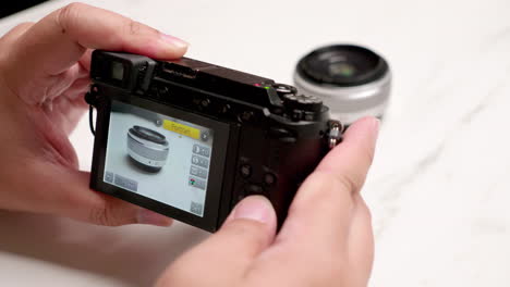 Close-up-of-an-individual-holding-a-point-and-shot-digital-camera-while-focusing-on-a-lens-on-a-table-and-adjusting-the-aperture-and-ISO-settings