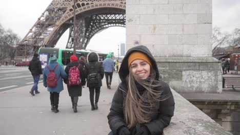 Female-tourist-portrait-smiling-in-front-of-the-eiffel-tower,-pedestrians-walking-pathway-Paris-city-centre