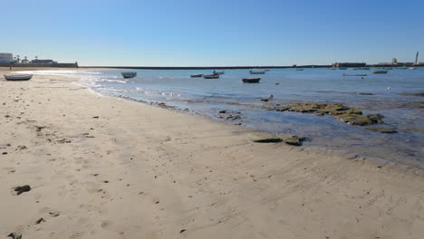 Small-boats-resting-on-the-sandy-shore-with-calm-sea-waters-in-Cádiz,-Spain