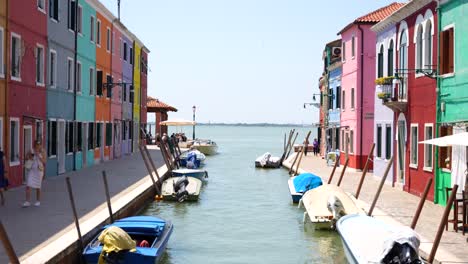 Two-female-tourists-strolling-along-canal-and-colorful-houses-in-Burano