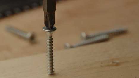 Close-up-of-drill-bit-of-electronic-screwdriver-being-placed-in-screw-and-drilling-it-into-wooden-board-in-slow-motion