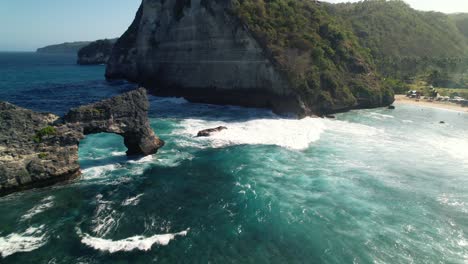 Natural-Rock-Arch-of-Nusa-Batupadasan-Island-and-Huge-Cliffs-Coast-of-Nusa-Penida,-Bali,-Indonesia---aerial-flyover