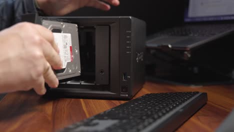 Person-inserting-a-hard-drives-into-a-small-black-computer-raid
