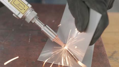 man-with-gloves-showcasing-laser-welding-device,-connecting-two-rectangular-pieces-of-sheet-metal-while-sparks-fly