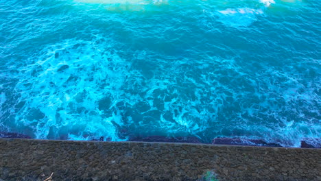 Leuchtende-Türkisfarbene-Meereswellen,-Die-Gegen-Eine-Ufermauer-In-Cádiz,-Spanien,-Krachen
