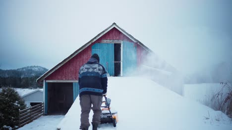 Vista-Posterior-De-Un-Hombre-Limpiando-Nieve-Fuera-De-Una-Granja-En-Noruega