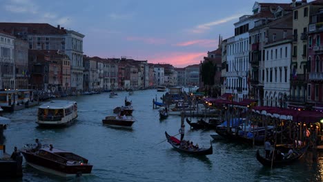 Sun-is-setting-behind-busy-Grand-Canal-with-gondolas,-motorboats-and-a-traghetto