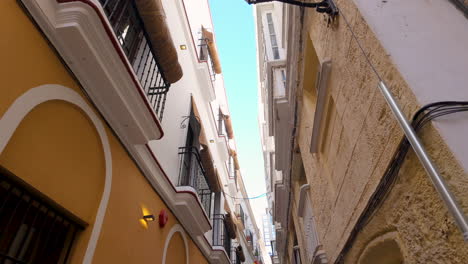 Upward-view-of-a-narrow-alley-with-traditional-facades-in-Cádiz,-Spain
