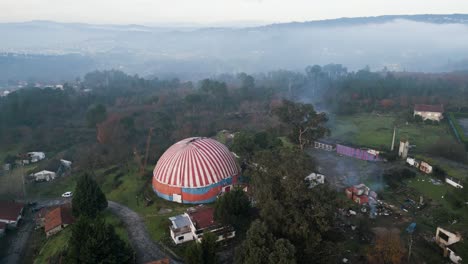 Drone-rises-above-Benposta-circus-tent-with-mist-on-treetop-canopy