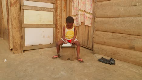 Africa-school-education-system,-black-children-kid-student-,-studying-alone-in-rural-remote-poor-undeveloped-village-taking-note-while-sitting-in-a-corner