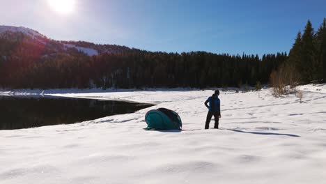 Man-throwing-quick-assemble-camping-tent-into-air-along-lake-snowy-banks-on-sunny-day