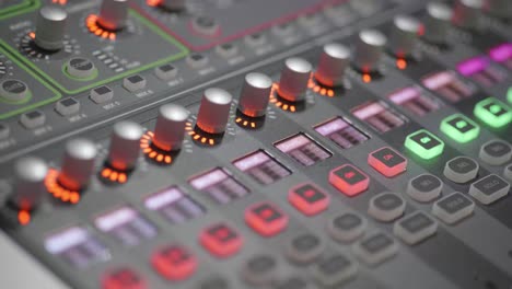 4k-close-up-of-professional-young-woman-adjusting-audio-levels-on-studio-mixer-console-with-colorful-dials