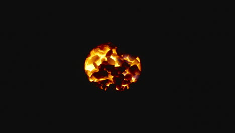 Coals-of-fire-glowing-in-the-dark-through-a-hole,-close-up-shot