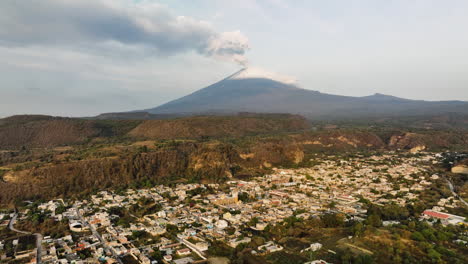 Aerial-view-rising-over-a-village-in-front-of-the-Popocatepetl-volcano,-in-sunny-Mexico