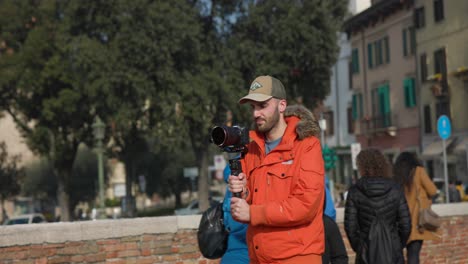 Male-Photographer-Holding-Camera-On-Gimbal-Stabilizer-While-Walking-On-The-Street-In-Verona,-Italy