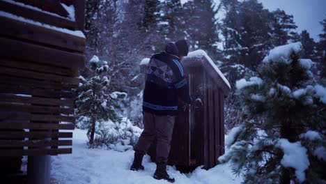 Man-Walks-Towards-Wooden-Smokehouse-Outdoor-In-Winter
