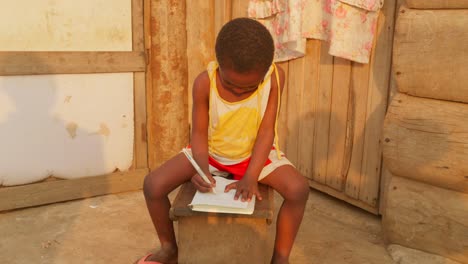 Schwarzafrikanische-Kinder-Lernen-Alleine-Und-Machen-Ihre-Hausaufgaben-In-Einem-Abgelegenen-Dorf-In-Afrika.-Kind-Schreibt-Und-Zeichnet-Mit-Stift-Auf-Einem-Notizbuch