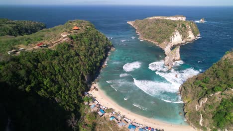Sand-Atuh-Beach-and-Lagoon-with-Rolling-Foamy-Waves-in-Nusa-Penida,-Bali,-Indonesia---Aerial-Pull-Back