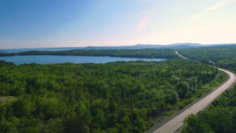 Smooth-drone-shot-over-the-trees-and-hydro-lines-revealing-a-highway-next-to-the-shimmering-blue-water-of-eastern-Canada