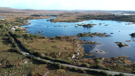 Aerial-drone-over-meadows-and-rocky-lakes-while-a-car-drives-down-furnace-road-galway-ireland