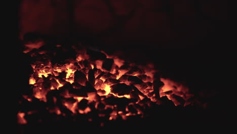 Fiery-coals-in-dark-stove,-nighttime-heat-source-close-up