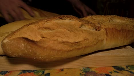 Hand-grabs-loaves-of-long-fresh-Galician-bread-to-stack-on-wooden-cutting-board