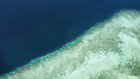 Shallow,-crystal-clear-water-transitioning-to-deeper-blue-ocean-and-coral-reef-in-Raja-Ampat,-West-Papua,-Indonesia,-aerial-drone-view