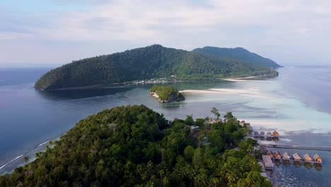 Luftaufnahme-Rückwärts-über-Regenwaldbedeckten-Tropischen-Inseln-Mit-Hütten-Am-Wasser-Mit-Blick-Auf-Das-Meer-Und-Korallenriffe-In-Raja-Ampat,-West-Papua,-Indonesien