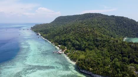 Aerial-drone-view-rising-over-white-sandy-beaches-and-remote-waterfront-huts-on-rainforest-covered-island-in-Raja-Ampat,-West-Papua,-Indonesia