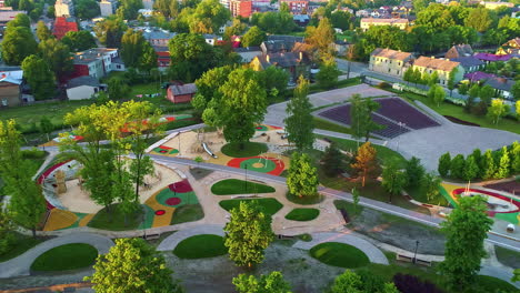Aerial-shot-of-a-vibrant-community-park-with-playgrounds-and-lush-greenery-during-sunset