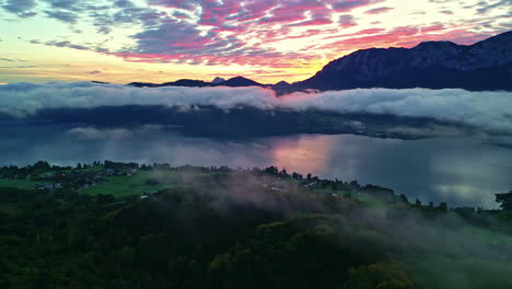 Aerial-view-of-Attersee-in-Austria-with-low-lying-colorful-clouds-at-sunrise,-lush-green-below