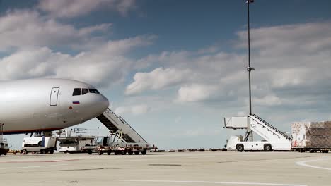 Commercial-airplane-at-the-gate-with-ground-support-equipment-and-cloudy-sky