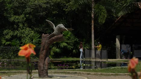 Estatua-De-Pájaro-Con-Una-Pareja-Tomando-Fotografías-Al-Fondo-En-El-Jardín-Botánico,-Cali,-Colombia