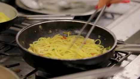 Chef-stirring-spaghetti-with-vegetables-in-a-pan-over-a-gas-burner