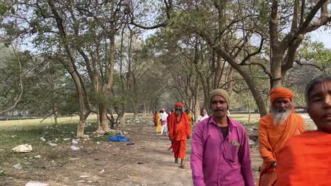 Front-view-of-Sadhus-walking-down-through-pathway-of-Maidan-during-afternoon-for-going-to-Ganga-Sagar-Mela-in-West-Bengal,-India