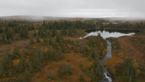 Drone-aerial-footage-of-a-stream,-lake-and-a-misty-forest-in-the-mountains-of-Sweden